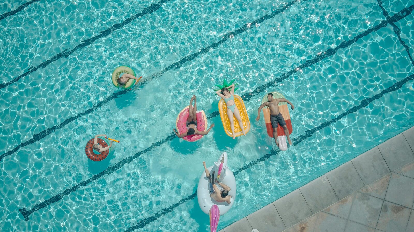 Patchworkfamilien im Urlaub. Zu sehen ist einPool mit Personen, die auf Schwimmtieren entspannen